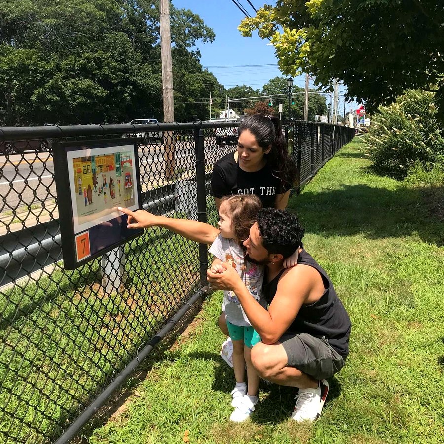 A family reading a StoryWalk panel mounted to a fence